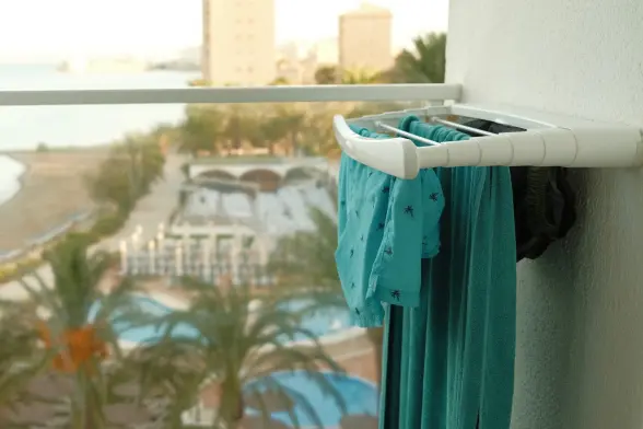 Swim trunks drying on a balcony rack overlooking a beach and palm trees.