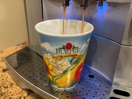 Two streams of espresso falling into a coffee mug illustrated with a yellow corn cob, a tomato, some flowers, and blue sky. Text says, "Burpee 125th Anniversary 1876-2001."