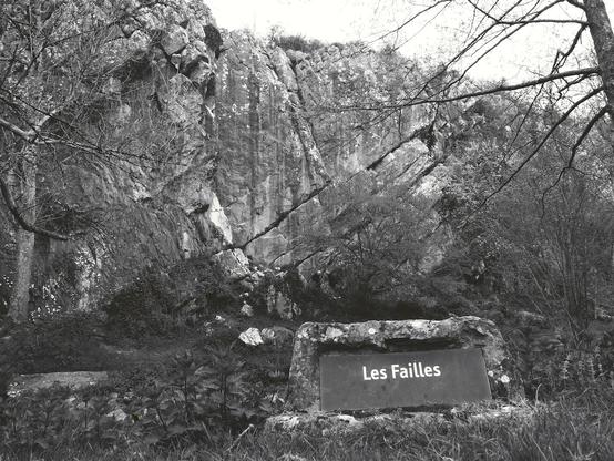 In the foreground, a stone sign reads "Les failles" ("The faults" in French). In the background, a large rock with fault lines.