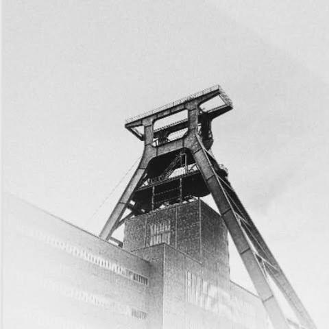 Schachtanlage eines ehemaligen Bergwerks mit Förderturm und Industriegebäude im Hintergrund.
