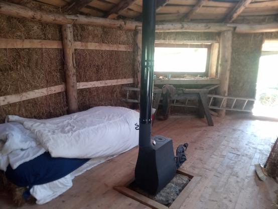 Inside the roundhouse. The floor is clear and swept, and there is a bed made up beside the stove.
