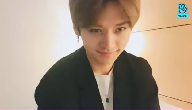 poor-quality image of Lee Know wearing a white t-shirt, dark blazer, and the green version from I.N's oval pendant collection