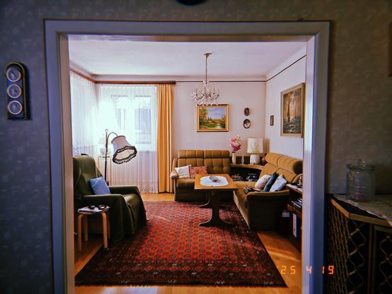A livingroom in retro design with a red carpet a reading lamp and a brown couch. Paintings on the wall.