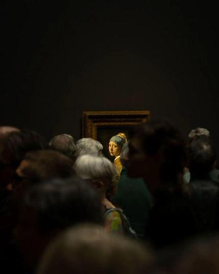 Im dunklen Raum versammelt sich eine Menschenmenge – Gesichter im Schatten, flüchtig, bewegt.
Doch aus der Tiefe des Bildes leuchtet ein einziges Gesicht still hervor:
Das Mädchen mit dem Perlenohrring von Vermeer.
Ihr Blick durchdringt die Zeit, scheinbar direkt auf dich gerichtet.
Unbeteiligt und doch wissend.
Sie sieht dich –
als wärst du derjenige, der sich erinnert.
Ein Auge im Zentrum des Vergessens.
Ein stiller Ruf aus einem anderen Jetzt.🖖