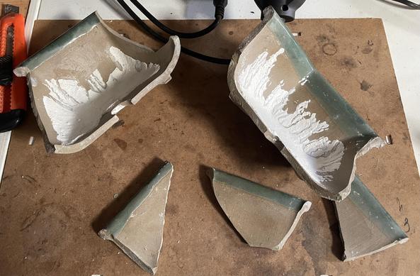 Una maceta de bonsái rota. Cinco piezas, dos grandes y tres pequeñas. La maceta es de cerámica, con un recubrimiento blanco interior y en los bordes se aprecia un esmaltado verde.