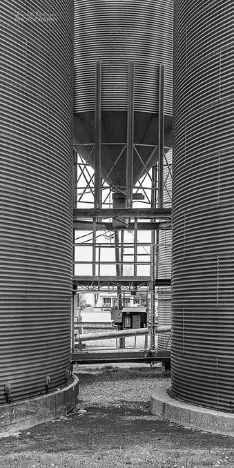 A view looking between two round metal silos at a smaller elevated metal silo .