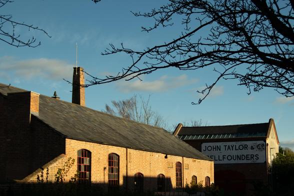 Bellfoundry buildings in the sun; the building on the back has a painted sign reading 'John Taylor & Co. Bellfounders'.