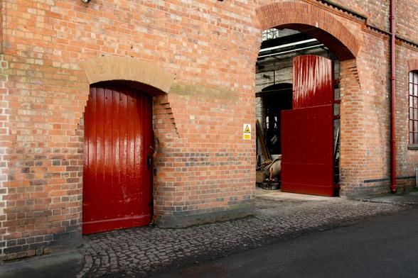 A red door and a red gate in the brick facade, showing the entrance to the Belffoundry's main workshop.
