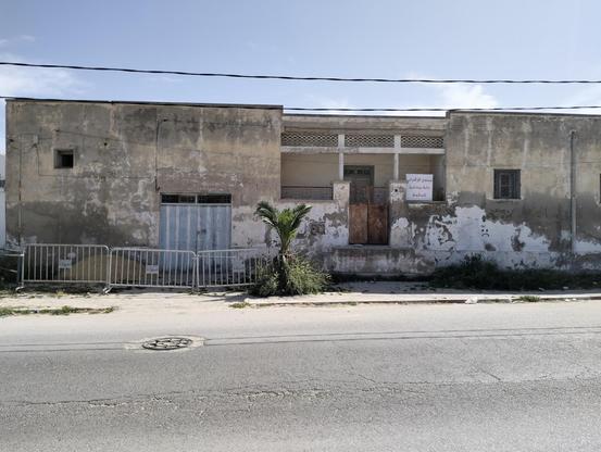 L'image montre une bâtisse ancienne et délabrée, avec des murs peints en blanc qui sont partiellement effacés, révélant une couche de couleur plus foncée. La façade présente des signes de détérioration, avec des zones de peinture écaillée et des taches. À gauche, une porte métallique bleue est fermée, tandis qu'à droite, une porte en bois sombre est également fermée. Un petit palmier est planté devant la porte, ajoutant une touche de verdure à l'ensemble. Un panneau blanc avec du texte en arabe est accroché à la façade avec "Interdiction de se rapprocher, la maison risque de s'effondrer". Des barrières métalliques sont installées devant la porte, suggérant une zone de restriction ou de sécurité. La rue devant la bâtisse est asphaltée, avec un couvercle de canalisation visible sur le côté. Le ciel est clair, indiquant une journée ensoleillée.

Fourni par @altbot, généré localement et en privé en utilisant Ovis2-8B

🌱 Énergie utilisée : 0.240 Wh