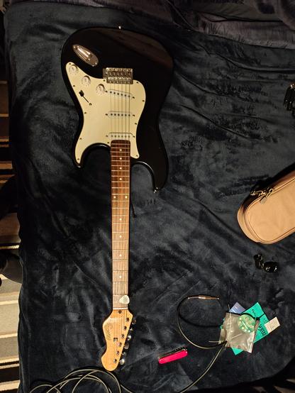 A black Stratocaster copy with a white pickguard. Background is a blue bedspread and the headstock says encore.