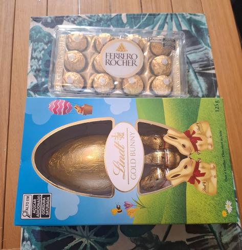 Em cima de uma mesa, vemos uma caixa com 12 bombons da Ferrero Rocher e uma caixa Gold Bunny da Lindt.