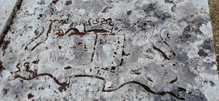 Une inscription sur une vieille pierre tombale. On distingue un livre, une couronne et deux lions