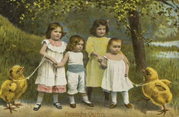 Vintage Easter postcard from the early 1900s showing four children dressed in formal, old-fashioned clothing. Two of them are holding leashes attached to oversized yellow chicks. The children are walking together hand in hand through a grassy field. The scene is whimsical, surreal, and slightly absurd.