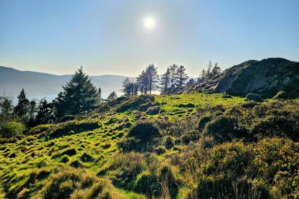A wide shot of a hilly, green landscape under a bright sun and blue sky in Ireland.