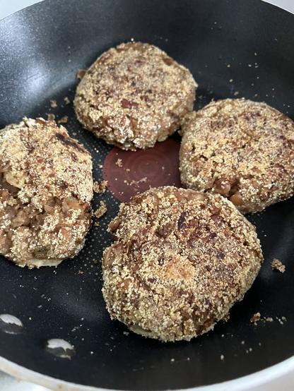 4 bean burgers coated with cornmeal in a small non stick frypan