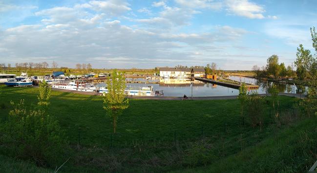 Panorama mariny. Po prawej i w centrum miejsce cumowania łodzi i innych jednostek pływających, po prawej płynie rzeka.