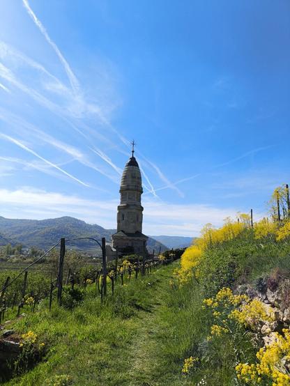 Ein Pfad führt über eine Wiese zu einem großen Denkmal. Blauer Himmel darüber.