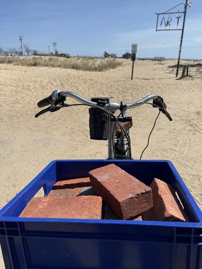The front of a Workcycles FR8 bicycle on the beach in Provincetown with a blue crate full of red bricks.