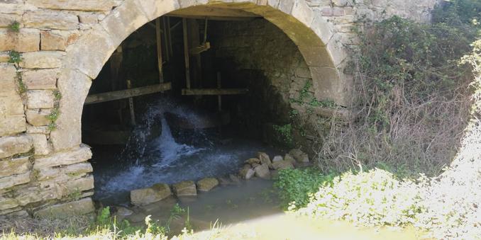 Vista mas cercana de la parte inferior del molino y su mecanismo externo, con compuertas y palas de madera.