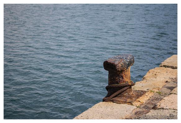 The image shows, in the foreground, a large mooring structure for ships in the port of Almería (Spain). The photo is divided into two parts: on one side, the solid concrete of the port, and on the other, the sea, a dark blue, still and placid on a sunny Sunday morning.
---
La imagen muestra en primer término un gran amarre para buques en el puerto de Almería. La foto está dividida en dos partes: por un lado, el hormigón macizo del puerto, y por otro, el mar, de un azul oscuro, quieto y plácido en una soleada mañana de domingo.