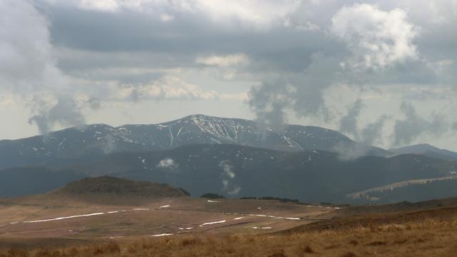 Blick über eine Hochgebirgswiese. 
Im Hintergrund eine Hochgebirgskette und graue Wolkenformationen darüber.