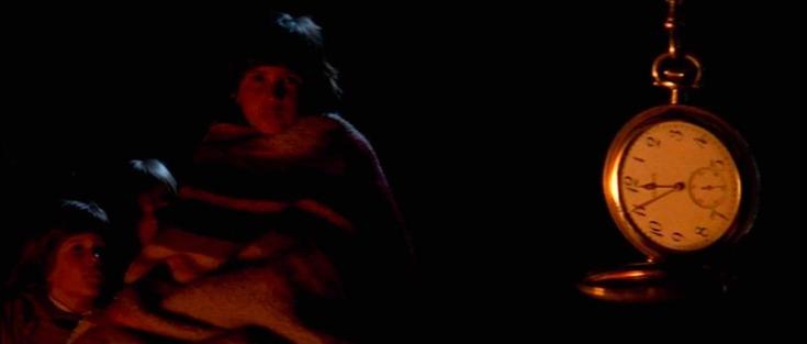 Children wrapped in blankets, their faces glowing from a fire. In the foreground, a pocketwatch spins, showing five minutes to 12.