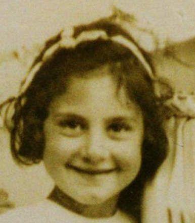 A photo of the face of a young smiling girl. She has a bit messy, dark hair.