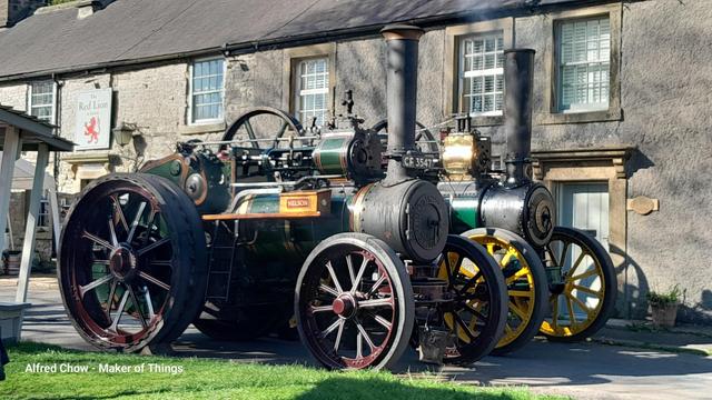 The same engines as in the previous image but seem from further back at a 3/4 front position. The Stone building behind can be seen in more detail, showing that it is a two storey building with upper floor sash windows glazed with eight small panes of glass per sash.

It can now be seen that the left side engine is painted in a darker green with deep burgundy wheels. A name place on the side of a wooden tool box says 'Nelson'. 

Both engines, though well kept and cleaned do still look like they have done work, and are not just polished museum pieces.
They are both in steam and are gently idling having just been parked there.