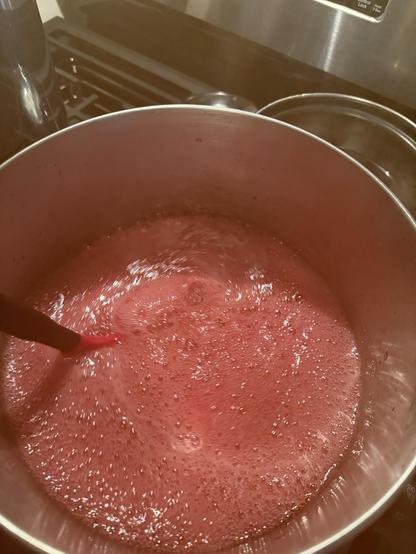 Stirring boiling pink foamy jelly in a stainless pot.