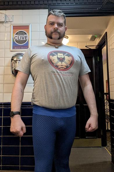 Me, in blue starchy leggings, and a grey top with a decal on the chest of a man chained up and a ball gag in his mouth.