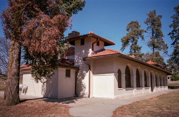 A Mission style building in brilliant white stucco catches the sun. Beside it a wind-damaged spruce whose rust colored leaves harmonize perfectly with the clay tile roof.