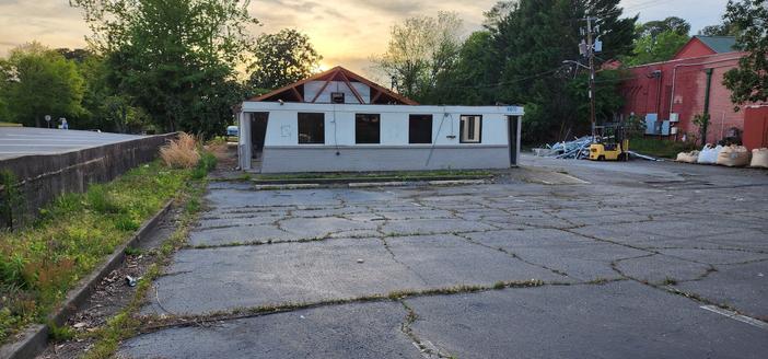 A parking lot with a white painted pizza hut from the 70s or 80s. Most of it's roof is missing