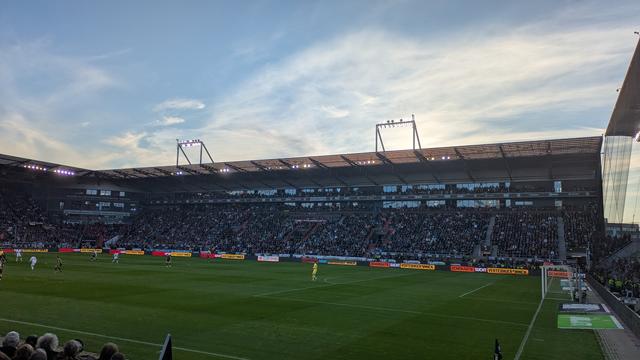 Stadion, Innenraum, das Spiel läuft. Als Bandenwerbung: "Demokratie sucht Verteidiger*innen"