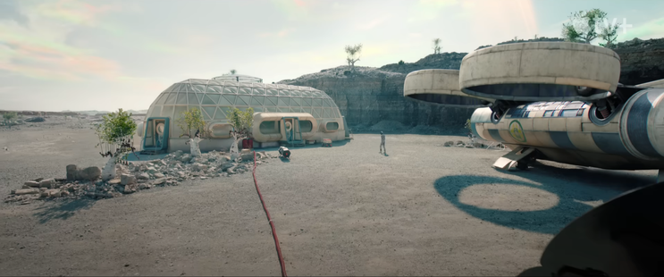 exterior wide show of a ship on the right of the frame and one of those settlement buildings with murderbot walking from the ship to the building.

the building looks like a long boat with triangular translucent bubbly panels on the side, and square like translucent panels on the rounded ends. there are a few trees and a red power line coming from the foregorund to it