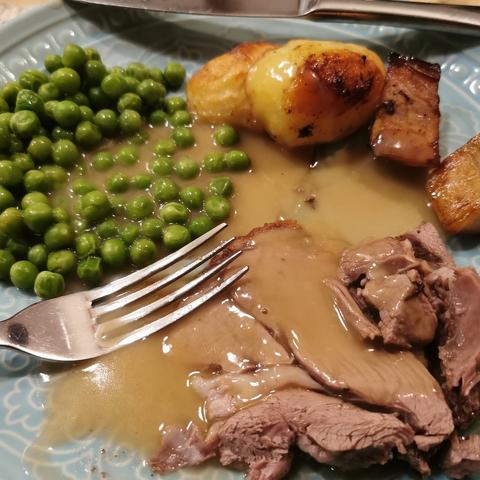 Turquoise plate with roast lamb, potatoes, kumara, peas and gravy, with a shiny fork in the middle