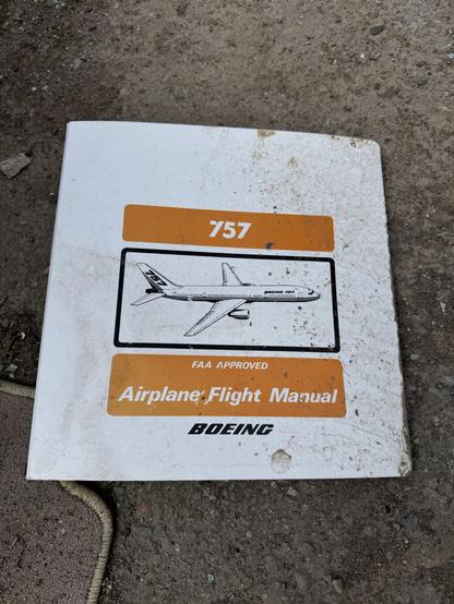 A dirty and worn Boeing 757 airplane flight manual lying on the ground. The cover features an illustration of the aircraft and text indicating it is FAA approved.