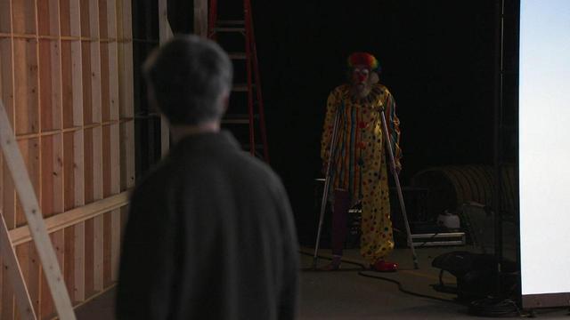Nathan in his studio lot looking at a clown in crutches at the end of a darkened hallway