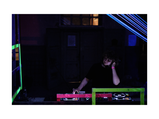 young person djing in low key club situation with fancy cubistic neon colored objects around