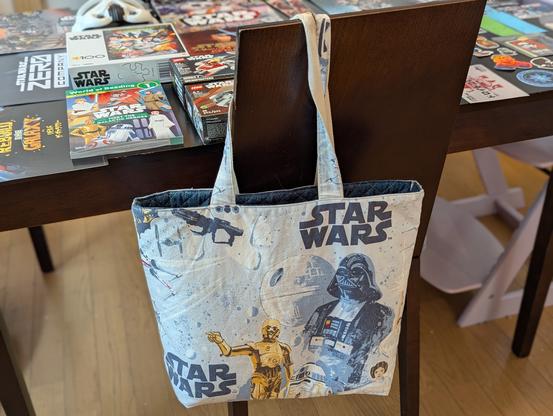 a handmade bookbag made from the classic  OG Star Wars bedsheets hanging on the back of a dining room chair.