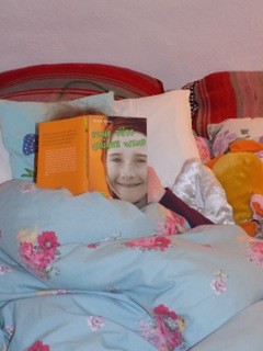 Foto von einem im Bett lesenden Mädchen. Das Gesicht wird vom aufgeschlagenen Buch verdeckt. Man sieht das Buchcover von EINE TÜTE GRÜNER WIND  - SOMMERFERIEN IN IRLAND.