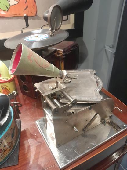 Appareil pour enregistrer des cartes postales sonores créé début XXz siècle. La machine a un corps en métal, avec un support où sera gravée la carte, il est surmonté d'un cône où l'on se penche pour prononcer le message.