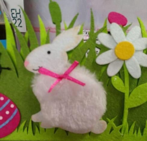 Eine österliche Landschaft aus Filz mit Ostereiern, Blumen, einem Marienkäfer und einem flauschigen weißen Osterhäschen mit einer rosanen Schleife
