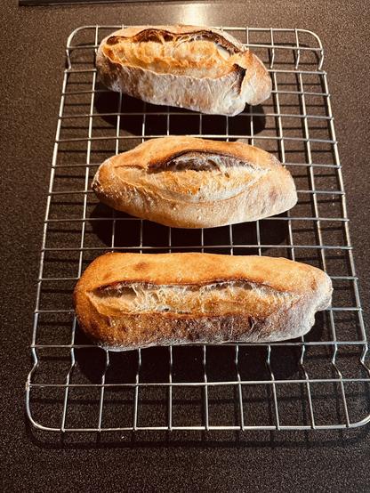 Three freshly baked baguettes are cooling on a wire rack.