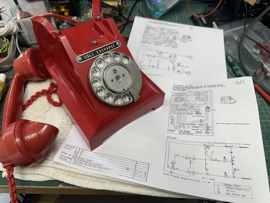 Red Bakelite dial telephone (British Tele 312) sat on the workbench with some schematic diagrams.