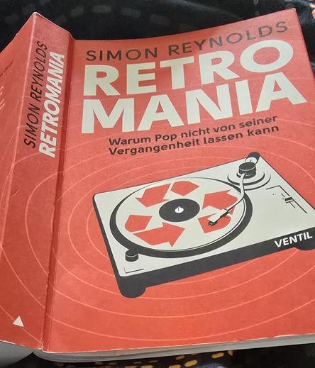 Buch Retromania
Darauf das Bild eines Plattenspielers, auf dem sich das Recycling Symbol dreht