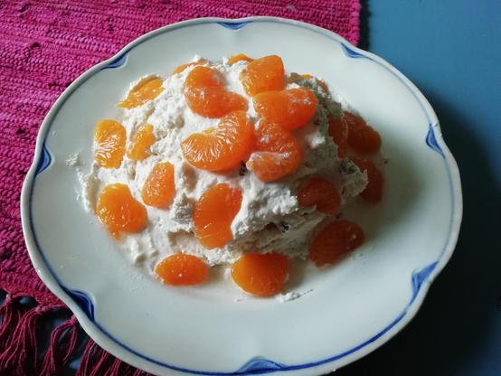 Valkoisella, sinikuvioisella lautasella on epämääräinen kasa pashaa, jonka päälle on aseteltu mandariininviipaleita.