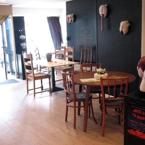 View inside the queer bar, with wooden tables and chairs and the sunlight falling through the door and windows.