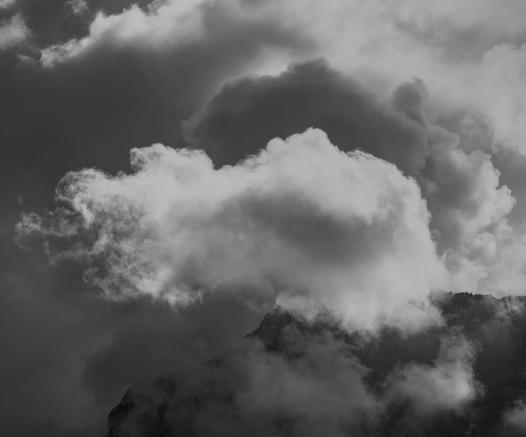 Photo d'une montagne quasiment entièrement cachée, d'énormes nuages, certains noirs, certains blancs, envahissent le ciel.