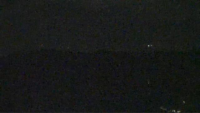 A dark image, the lower half slightly darker than the upper half. There are a scattering of small lights in the distance. Image is overall staticky.