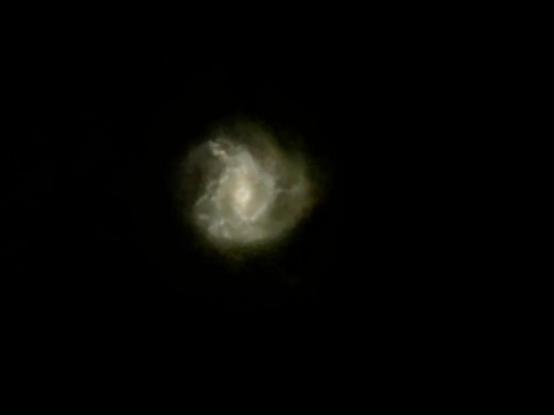 A golden glowing barred spiral galaxy against a black field. The spirals of the galaxy are surrounded by an extended glowing cloud.